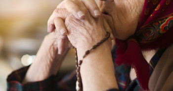 idosa segurando um terço entre as mãos, mostrando sua espiritualidade